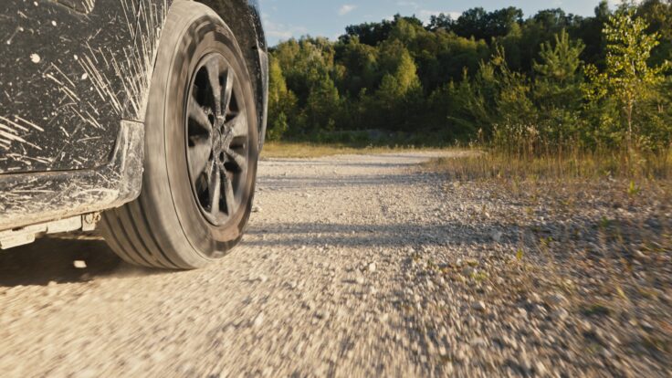 Close Up Of A Car Driving On A Dusty, Rocky Dirt Road