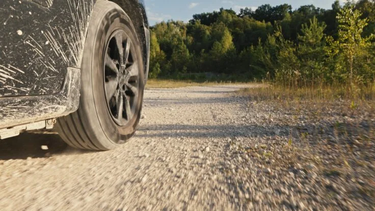 Close Up Of A Car Driving On A Dusty, Rocky Dirt Road